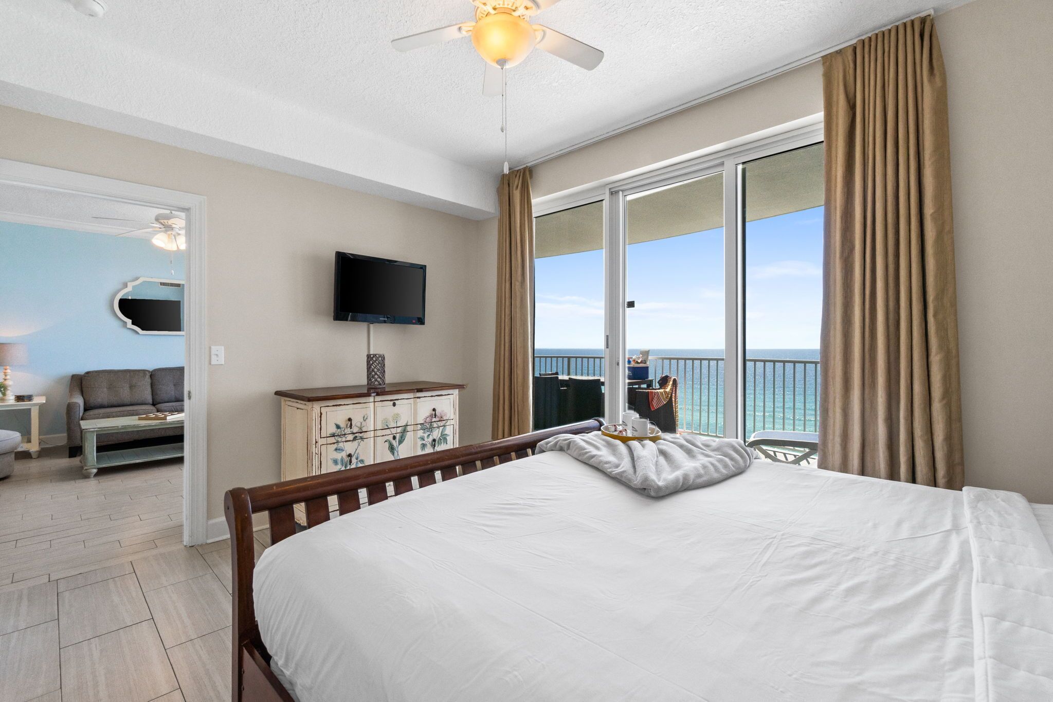 Hotelkamer met een bed, televisie, dressoir, stoel en balkon met uitzicht op de oceaan.