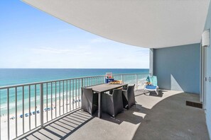 A balcony with a view of the beach, a table with chairs, and a sun lounger.