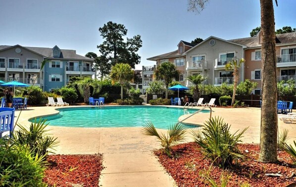 Relax by the resort's central pool surrounded by lush greenery and lounge chairs.