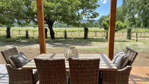 Un espacio exterior cubierto para comer con mobiliario de mimbre y vistas a un viñedo.