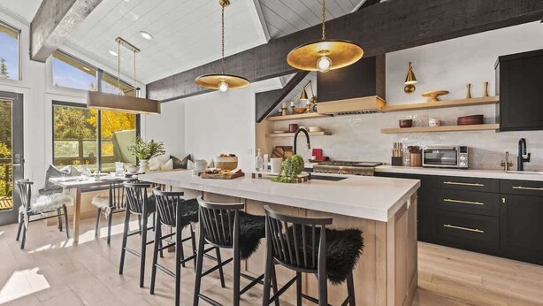 Una cocina moderna con una isla central, taburetes de bar, iluminación colgante y vistas al exterior.
