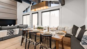 Un comedor con una mesa de madera dispuesta para cuatro personas, un sofá y un ventanal grande.
