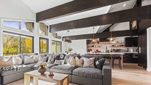 Una sala de estar moderna con un amplio sofá seccional gris, una mesa de centro de madera y una zona de cocina con armarios oscuros y una barra.
