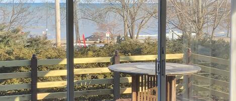 A deck with a wooden table and bench, overlooking a beach with trees and a distant view of the sea.