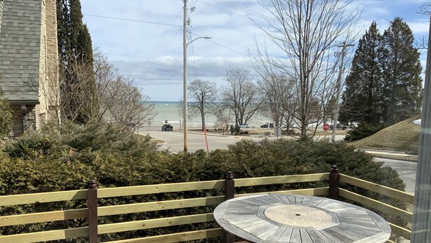 A wooden deck with a round table and a view of a road and beach. - BEACHVIEW GETAWAY (Sheboygan)