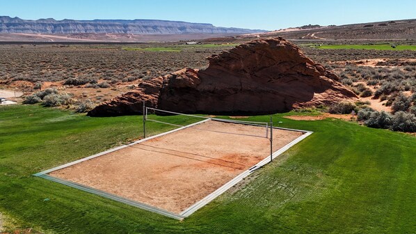 A tennis court with a net, surrounded by green grass and a large rock formation in the background. - Elevated Vista: Golf View + Resort Access + Large Groups (Hurricane)
