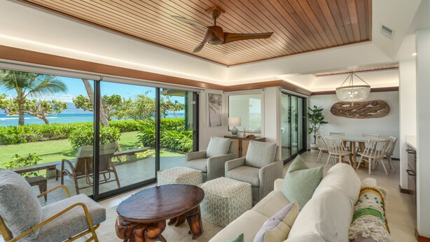 A spacious living area with a large sliding glass door leading to a balcony with a view of the ocean. There are multiple seating options including a sofa, chairs, and a dining table. - Oceanfront luxury 3bd condo on Baby Beach (Lahaina)