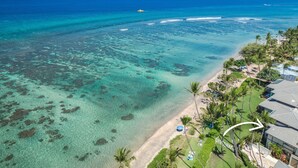 An aerial view of a beach with clear turquoise waters, a sandy shore, and a row of houses with a view of the ocean. - Oceanfront luxury 3bd condo on Baby Beach (Lahaina)