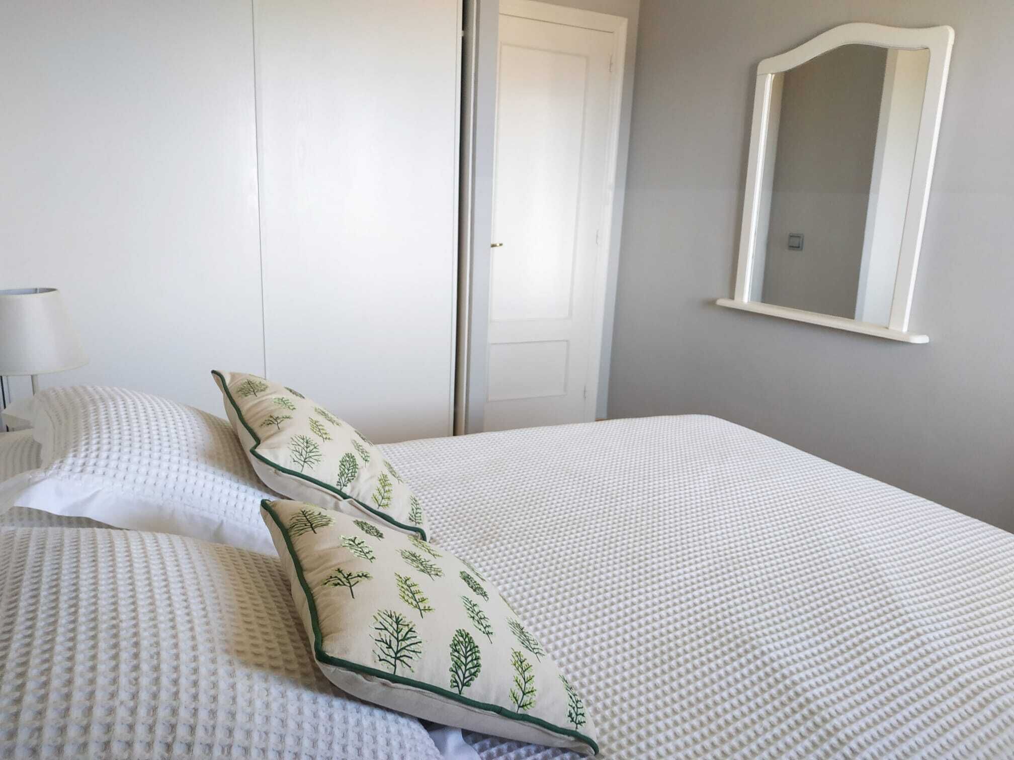 A neatly made bed with white bedding and two pillows with a leaf pattern.