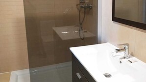 Une salle de bain moderne avec une douche à l’italienne en verre, un lavabo blanc et un meuble-lavabo foncé.