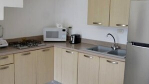 Een moderne keuken met lichte houten kastjes, een roestvrijstalen koelkast, een magnetron en een gasfornuis.
