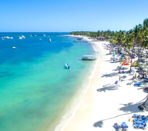 Enjoy a serene beach experience with turquoise waters, palm trees, and comfortable lounge chairs.