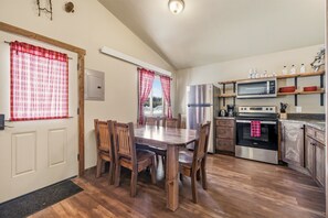 Een kleine keuken met een eettafel, houten stoelen, een koelkast, een magnetron en een oven.