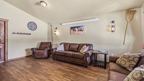 A living room with a brown leather sofa, a brown leather armchair, and a wooden coffee table. There is a clock on the wall and a painting above the sofa.