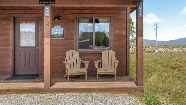 A wooden cabin with a porch, two Adirondack chairs, a door, and a window.