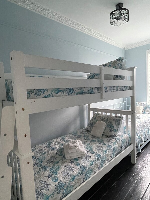 A bunk bed with a floral bedspread, a white headboard, and a window with blinds.