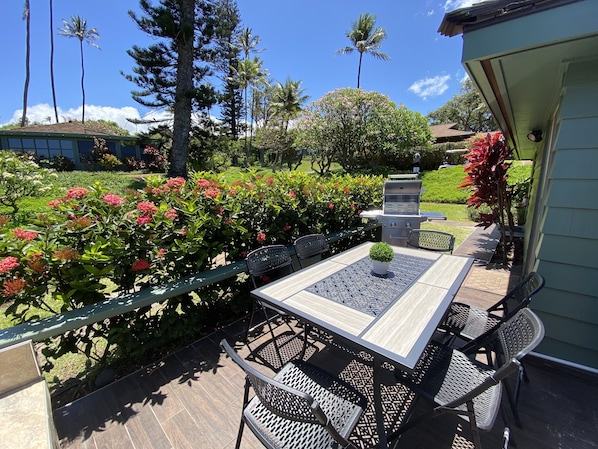 An outdoor patio with a table and chairs, surrounded by lush greenery and flowering plants.