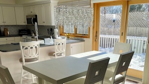 Un coin repas avec une table et des chaises, une cuisine en arrière-plan et une vue sur une terrasse en bois.
