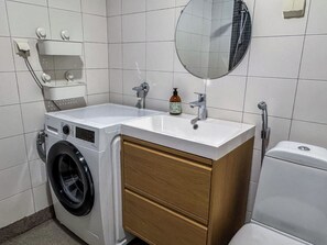 Une petite salle de bain équipée d’un lave-linge, d’un lavabo, d’un miroir et de toilettes.
