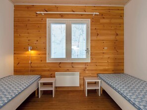 A room with two single beds, a small table, a heater, and a window with blinds.