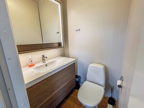 Une salle de bain avec un lavabo blanc, un miroir, des toilettes et une poubelle.
