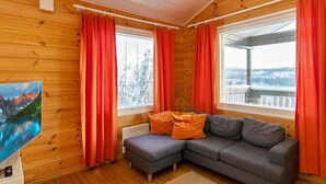 A cozy cabin room with a grey sectional sofa, red curtains, and a painting of a mountain landscape. - Hallan paroni b paritalo by Interhome (Hyrynsalmi)