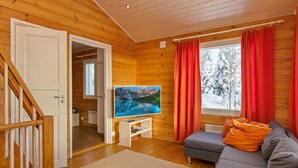A cozy cabin interior with a wooden interior, a television on a stand, a gray sofa with orange cushions, and a window with red curtains. - Hallan paroni b paritalo by Interhome (Hyrynsalmi)