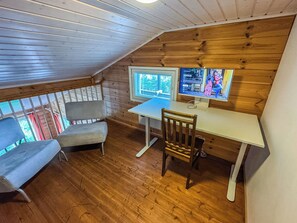 Une pièce mansardée chaleureuse avec un plafond en bois, un bureau avec un ordinateur, une chaise et un banc rembourré.