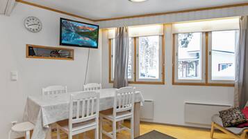A dining area with a table, chairs, a television, and a window with curtains.