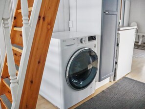 A modern laundry room with a front-loading washing machine, a grey cabinet, and a wooden staircase.