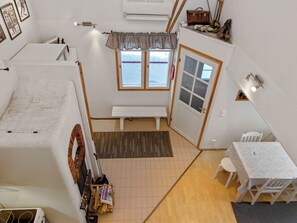 A compact room with a bench, a table, a window with curtains, and a door.