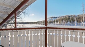 A covered outdoor area with a snow-covered deck and a view of a snowy landscape with trees and a hill.