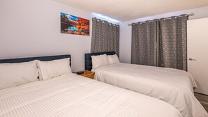 Una habitación doble con dos camas, una mesita de noche, un cuadro en la pared y cortinas estampadas.