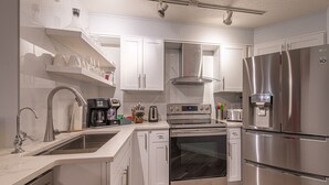 Una cocina moderna con armarios blancos, electrodomésticos de acero inoxidable, horno empotrado y refrigerador.