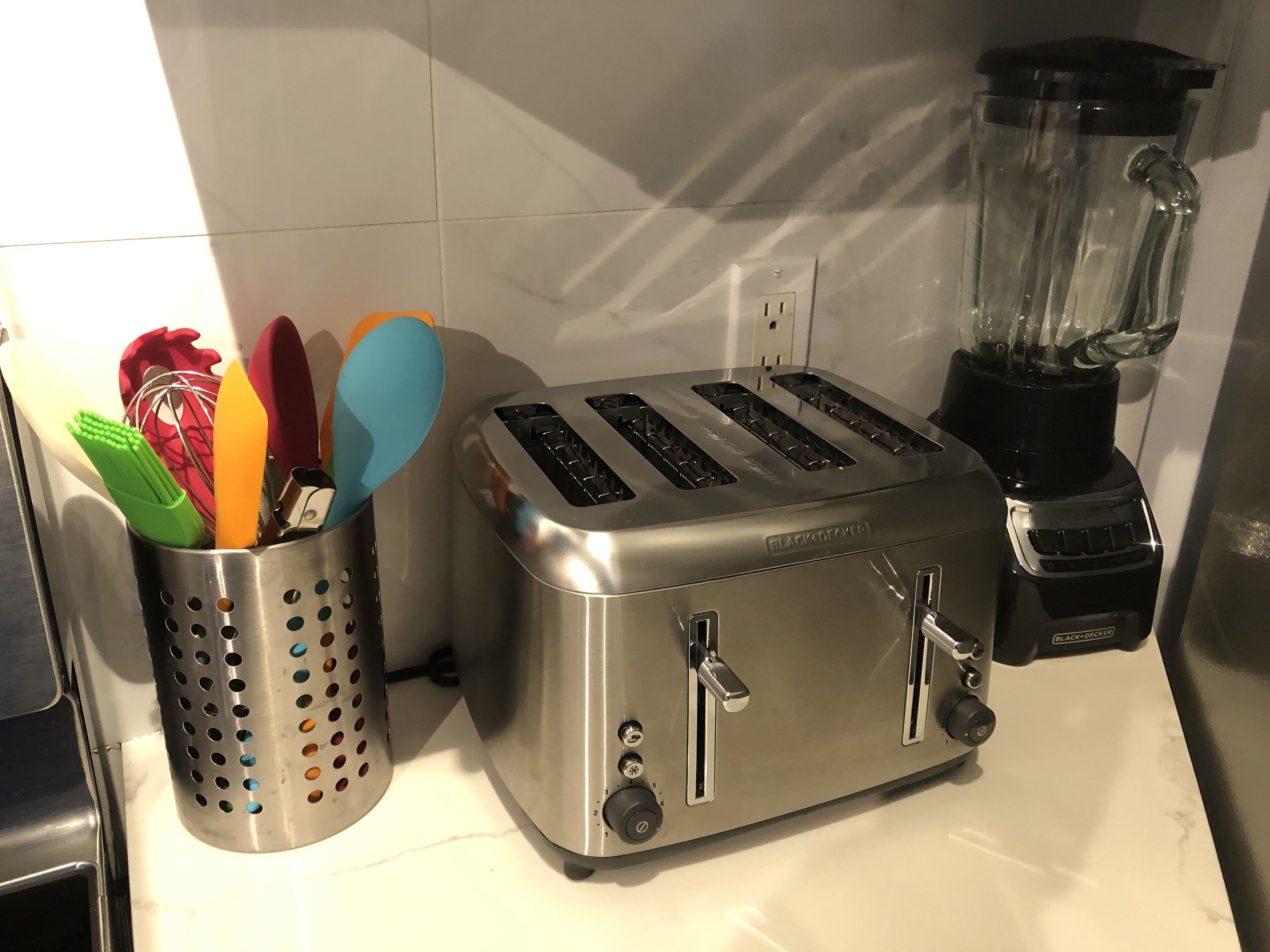Eine Küche mit einem Edelstahl-Toaster, einem Mixer und einem Besteckhalter voller bunter Küchenhelfer.