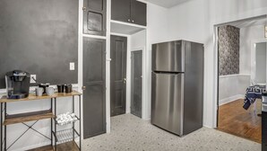 Une cuisine compacte équipée d’un réfrigérateur en acier inoxydable, d’une machine à café et d’une table en bois recouverte d’une nappe à motifs.