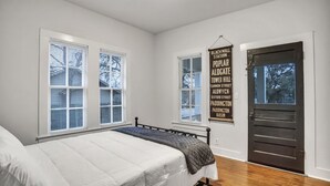 Une chambre à coucher avec un lit, deux fenêtres, une porte et un panneau décoratif sur le mur.