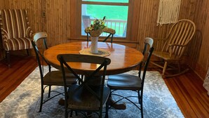 A dining area with a round wooden table, six chairs, a vase with flowers, and a wooden wall with a window. - Visit the farm! (Dekalb)