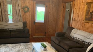 A living room with wooden walls, a wooden floor, two dark brown sofas, a light wooden coffee table with a plant, and a grey rug. - Visit the farm! (Dekalb)