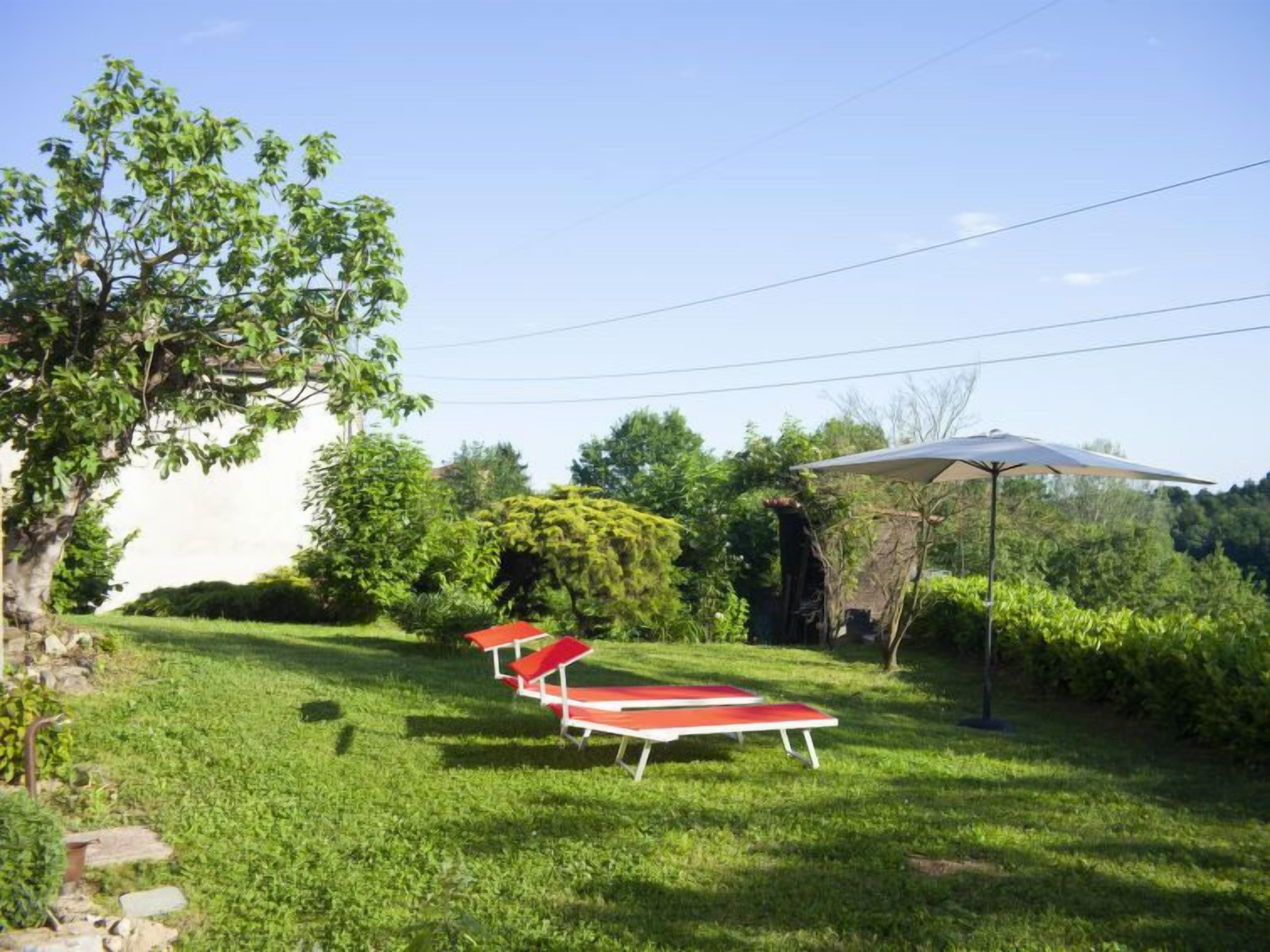 Un'area verde all'aperto con tre poltrone rosse e un ombrellone grande.