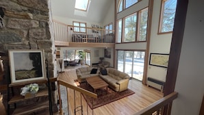 A spacious living area with a stone wall, a wooden staircase, and a large window overlooking a snowy landscape. - Stunning Private Lakehouse with Dock and outdoor Hot Tub (Manchester)