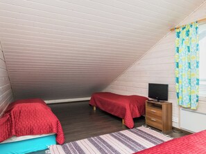 A small, sloped-roofed room with two beds, a television, and a wooden dresser.