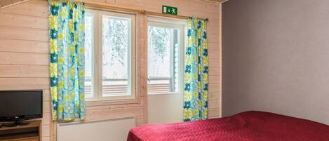 Ein Schlafzimmer mit einem Bett, einem Fernseher auf einem Holztisch und einem Fenster mit Vorhängen.