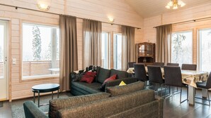 A spacious living area with a sofa set, a dining table with chairs, and large windows with curtains.