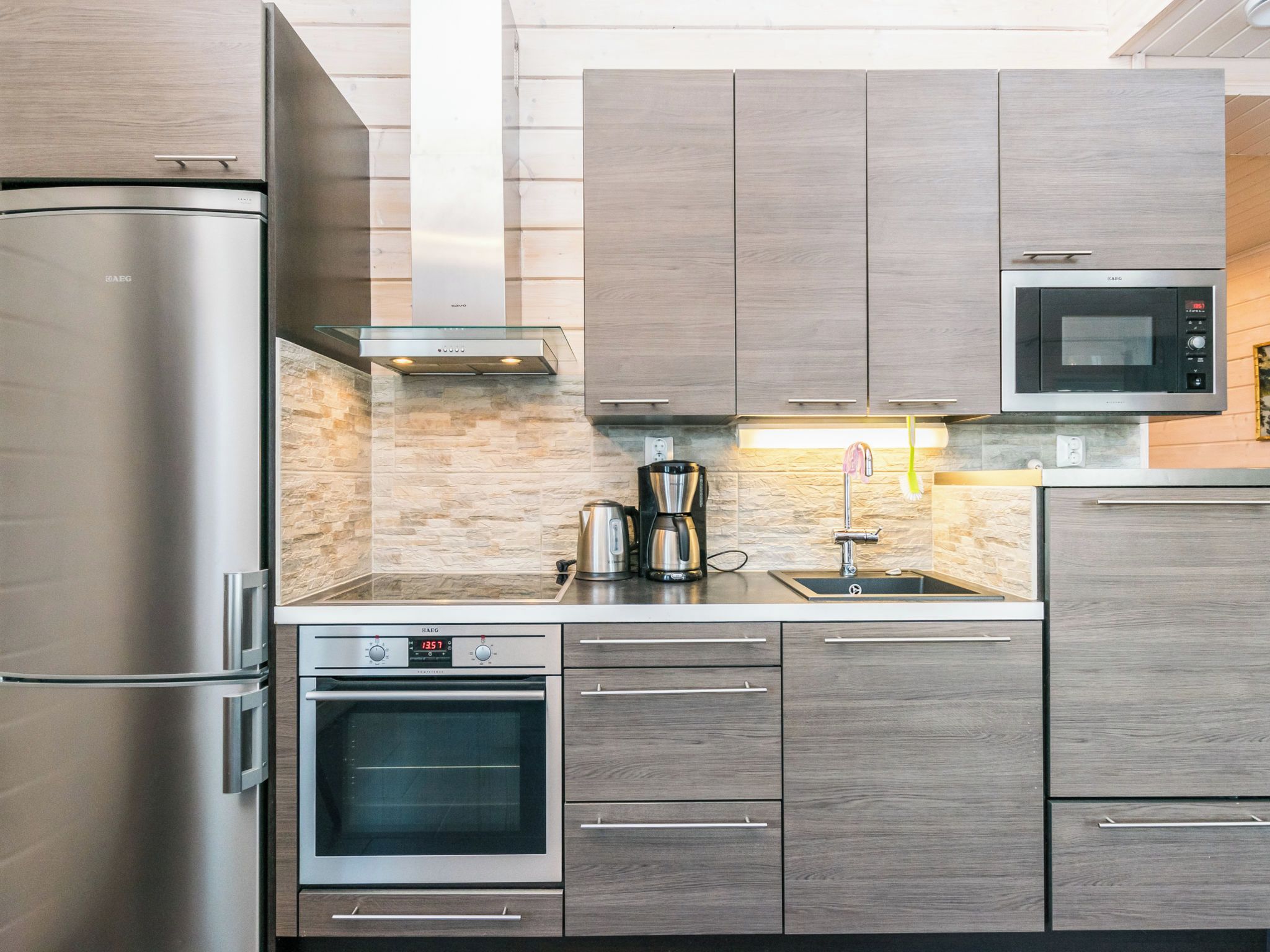 Una cucina moderna con elettrodomestici in acciaio inossidabile, mobili in legno e una parete di fondo in pietra.