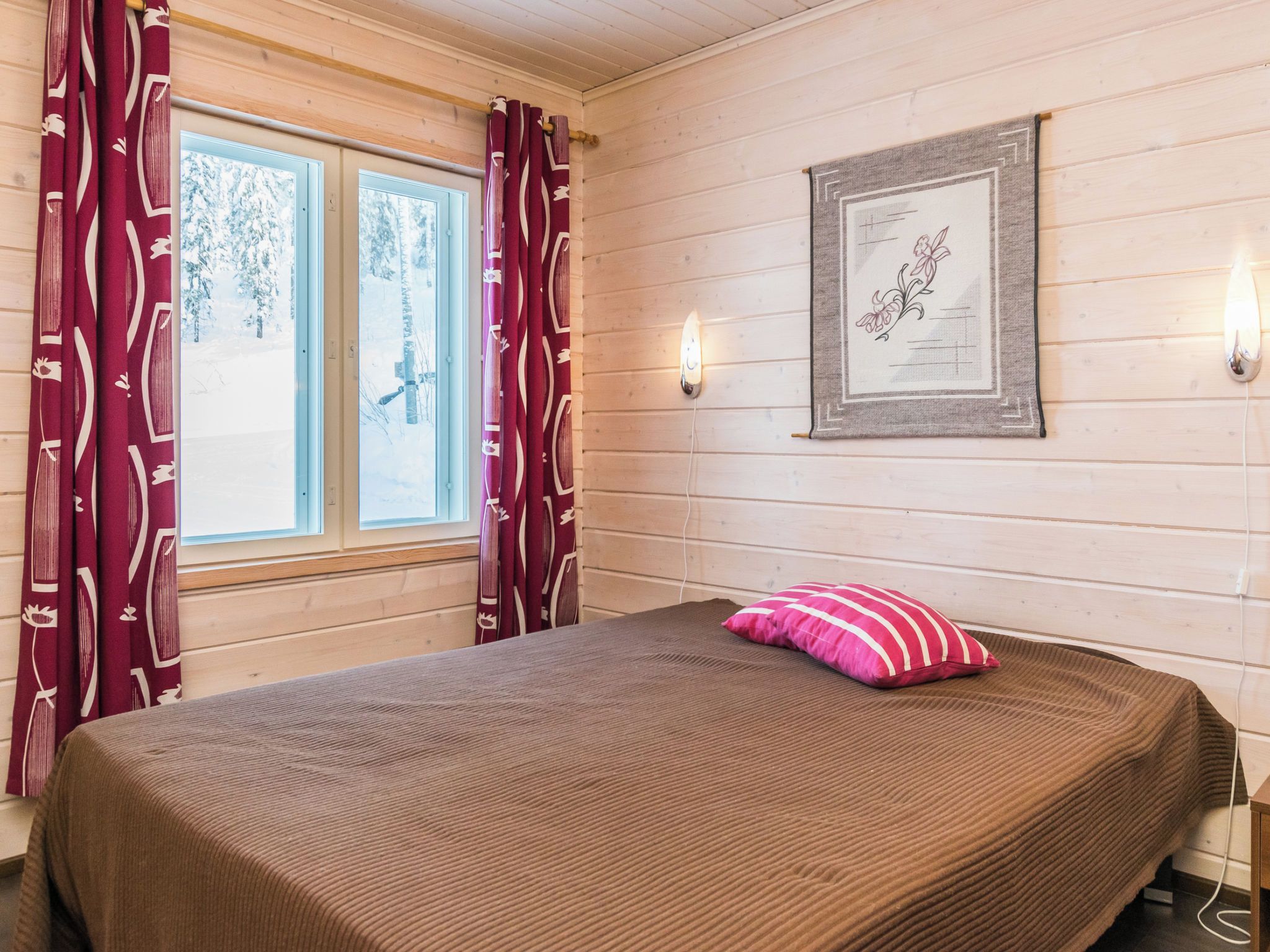 Una habitación con una cama, una ventana con cortinas, una lámpara de pared y un cuadro enmarcado.