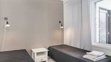 A modern bedroom with two beds, a small white nightstand, and a window with curtains.