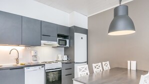 Una cocina moderna con armarios grises, un lavavajillas blanco, una estufa y un microondas. Hay una mesa de comedor con sillas blancas y una lámpara colgante.