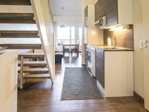 A modern kitchen with a built-in microwave, a stainless steel sink, and a wooden staircase leading to a dining area.