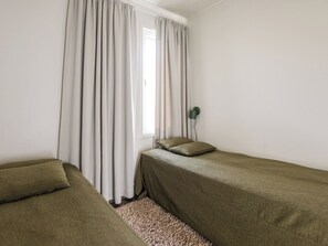 Une chambre simple avec deux lits simples, une fenêtre avec des rideaux et une lampe verte.